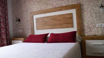 A bed with a wooden headboard, two red pillows, and a white quilted bedspread.