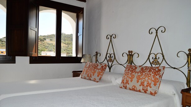 A double bed with ornate metal headboard, two pillows with orange patterns, and a window with a view of a hilly landscape. - 2 bedroom apartment (Aliseda)