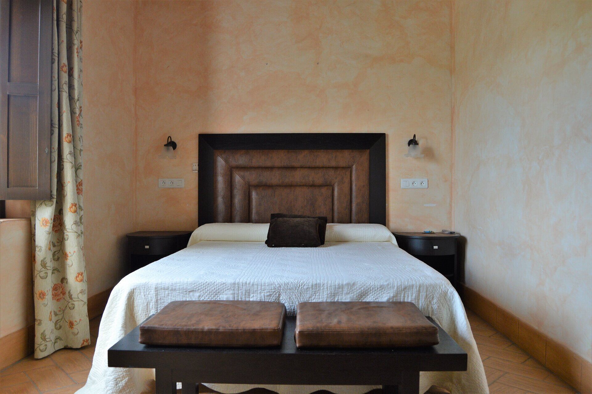 Un dormitorio con una cama grande, dos mesitas de noche, un cabecero de madera y una cortina con estampado floral.