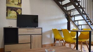 A modern living room with a wooden table, yellow chairs, a flat-screen TV on a cabinet, and a staircase. - 2 bedroom apartment (Aliseda)