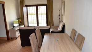 A dining area with a wooden table and four chairs, a sofa, and a small side table with a vase. - 2 bedroom apartment (Aliseda)