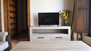 A living room with a flat-screen TV on a wooden stand, a vase with dried flowers, and a wooden cabinet. - 2 bedroom apartment (Aliseda)