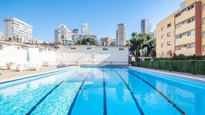 Une piscine intérieure à l’eau d’un bleu limpide, entourée de bâtiments, avec une vue sur la ville en arrière-plan.