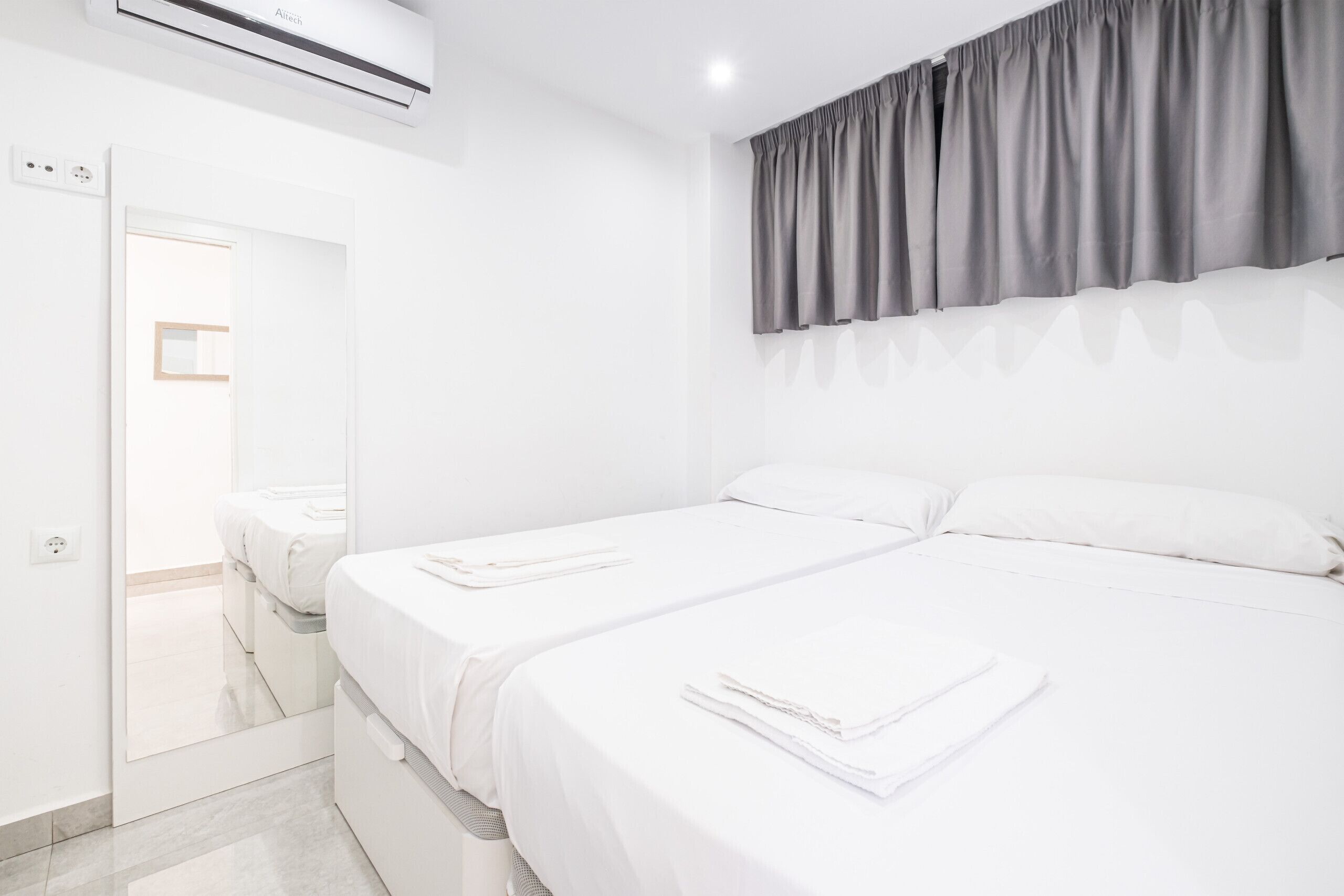 Een hotelkamer met twee bedden, een grote spiegel en een grijze gordijn.