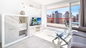 Un salon moderne avec un téléviseur, une table en verre et un balcon offrant une vue sur la ville.