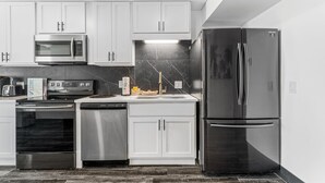 A modern kitchen with white cabinets, stainless steel appliances including a microwave, oven, dishwasher, and refrigerator, and a marble backsplash. - The Summit 132 (Panama City Beach)