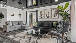 A modern living room with a grey sectional sofa, a black leather sofa, a glass coffee table, and a large potted plant. - The Summit 132 (Panama City Beach)