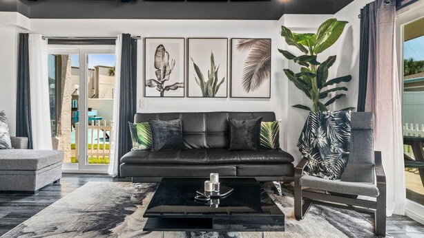 A modern living room with a black leather sofa, a glass coffee table, and framed botanical prints on the wall. - The Summit 132 (Panama City Beach)