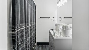 A bathroom with a shower curtain, towel rack, and a vanity with a mirror and lights. - The Summit 132 (Panama City Beach)