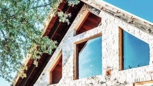 A stone house with a sloped roof, large windows, and a front door with a decorative arch.