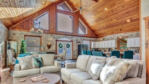 A spacious living room with a high wooden ceiling, stone walls, and a large window.