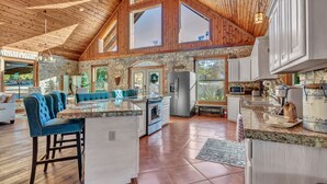 A spacious kitchen with a large island, stone walls, and wooden ceiling beams.