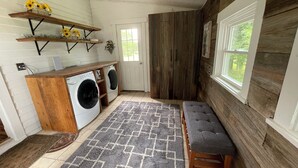 Un cuarto de lavandería con lavadora, secadora, banca de madera, alfombra y estantes con flores.