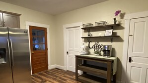Una cocina con un refrigerador de acero inoxidable, piso de madera, una estación de café con cafetera, y una puerta con ventana.