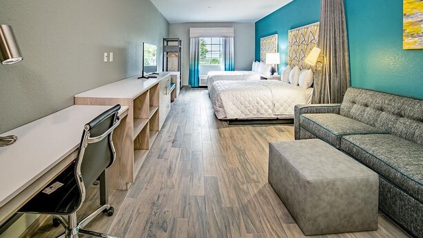 Habitación de hotel con escritorio, dos camas, un sofá y un ventanal grande.