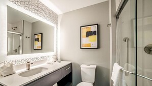 Un baño moderno con un espejo grande, dos lavamanos, un inodoro y una cabina de ducha con paredes de vidrio.