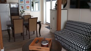 Ein modernes Wohnzimmer mit einer Couch, einem Esstisch mit Stühlen, einem an der Wand befestigten Fernseher und einem Kühlschrank.