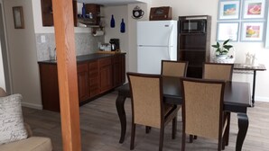 Eine moderne Küche mit Holzschränken, einem Kühlschrank und einer Mikrowelle. Ein Esstisch mit vier Stühlen steht daneben.