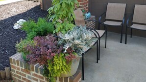 Ein Ziegelpflanzgefäß mit verschiedenen Pflanzen, ein Metallstuhl und eine Beton-Terrasse.