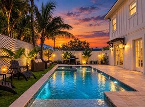 Una piscina con vistas a un atardecer, rodeada de palmeras y mobiliario de exterior.