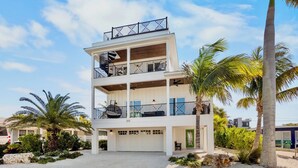 A multi-story building with a white exterior, balconies, and a garage. - Paradise Bound! Backyard Bliss with Sun Shelf, BBQ and Coastal Decor (Anna Maria)