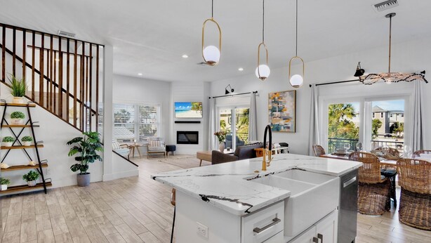 A modern kitchen with a large island, wooden staircase, and dining area with wicker chairs. - Paradise Bound! Backyard Bliss with Sun Shelf, BBQ and Coastal Decor (Anna Maria)