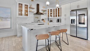 A modern kitchen with white cabinetry, a central island with stools, stainless steel appliances, and pendant lighting. - Paradise Bound! Backyard Bliss with Sun Shelf, BBQ and Coastal Decor (Anna Maria)