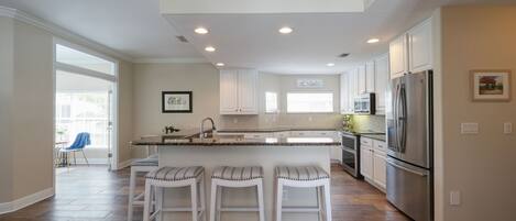A modern kitchen with white cabinets, a stainless steel refrigerator, and a central island with bar stools.
