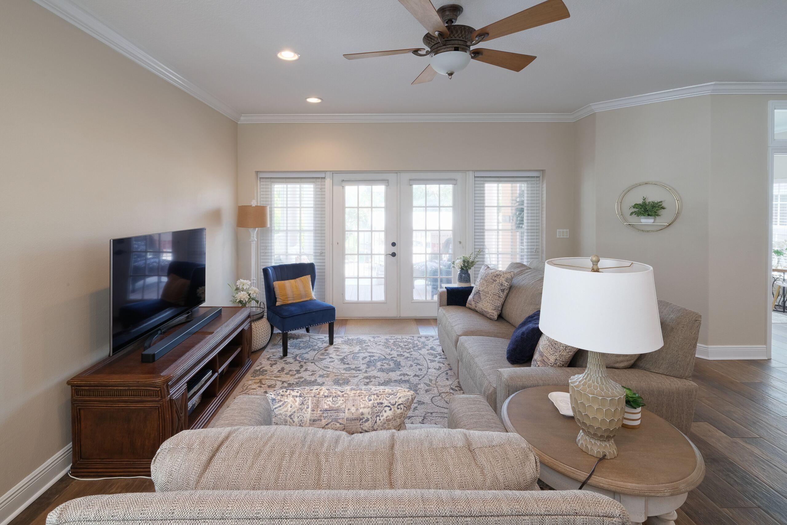 Un salon comprenant un téléviseur, un ventilateur de plafond, un canapé, une table basse et un tapis à motifs.