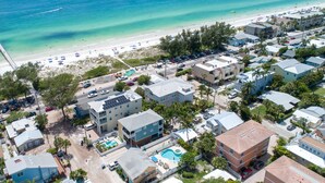 An aerial view of a coastal residential area with a beach, houses, and a swimming pool.