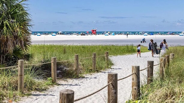 Een zandpad langs het strand, met houten palen en een redershut in de verte.