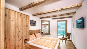 Een slaapkamer met een houten bed, een houten garderobe, een stoel en een groot raam met uitzicht op een besneeerd landschap.