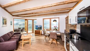 Een moderne keuken met houten balken, een eethoek met uitzicht en een woonkamer met een bank en een tafel.
