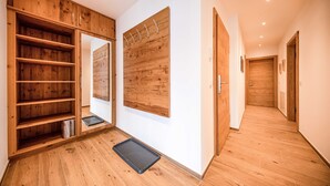 Een hal met houten vloeren, een grote spiegel en een houten garderobe met meerdere planken.