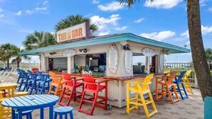 A tiki bar with colorful chairs and tables, a menu board, and a sign reading "TIKI BAR". - The Summit 1121 (Panama City Beach)