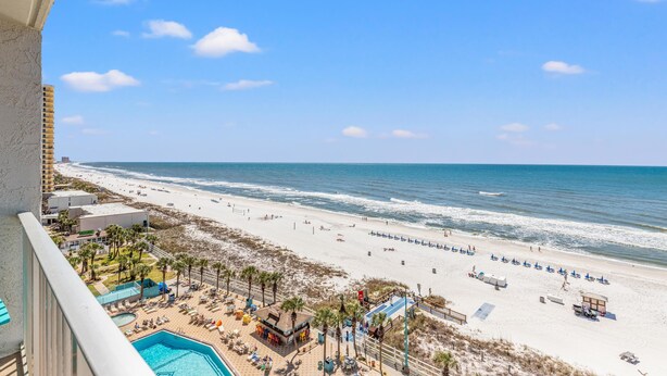 A beach view from a balcony with a pool, beach umbrellas, and a lifeguard tower. - The Summit 1011 (Panama City Beach)