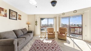A spacious living room with a grey sofa, two armchairs, a patterned rug, and a balcony with a city view.