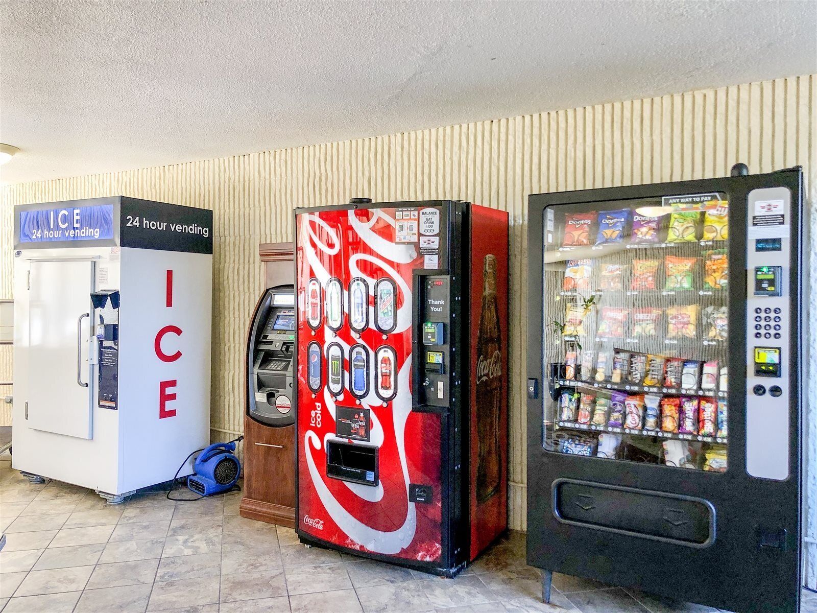 A vending area with an ice machine, a Coca-Cola branded drink dispenser, and a snack vending machine.