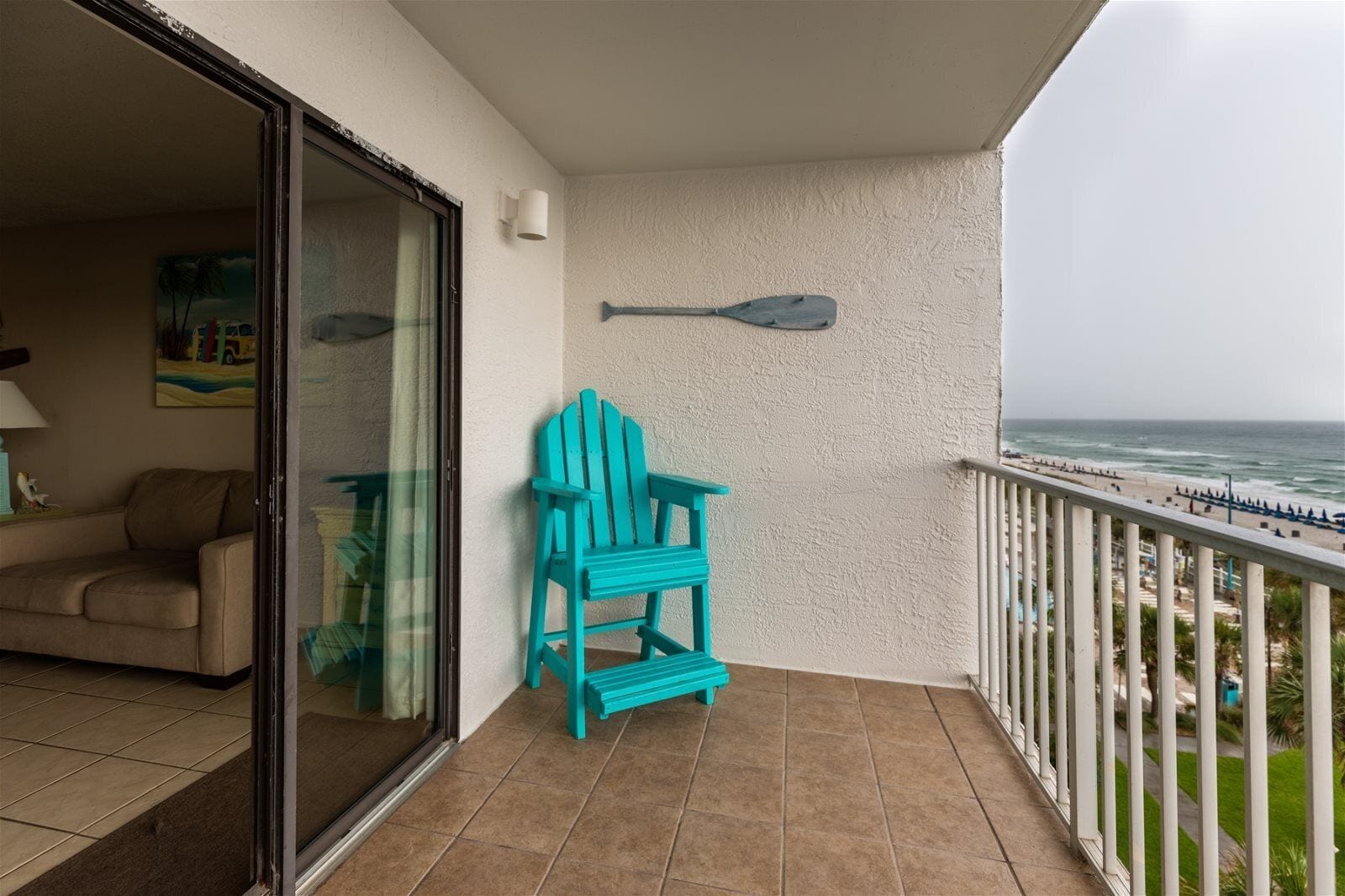 Uma varanda com uma cadeira Adirondack turquesa, uma parede branca e vista para o oceano.