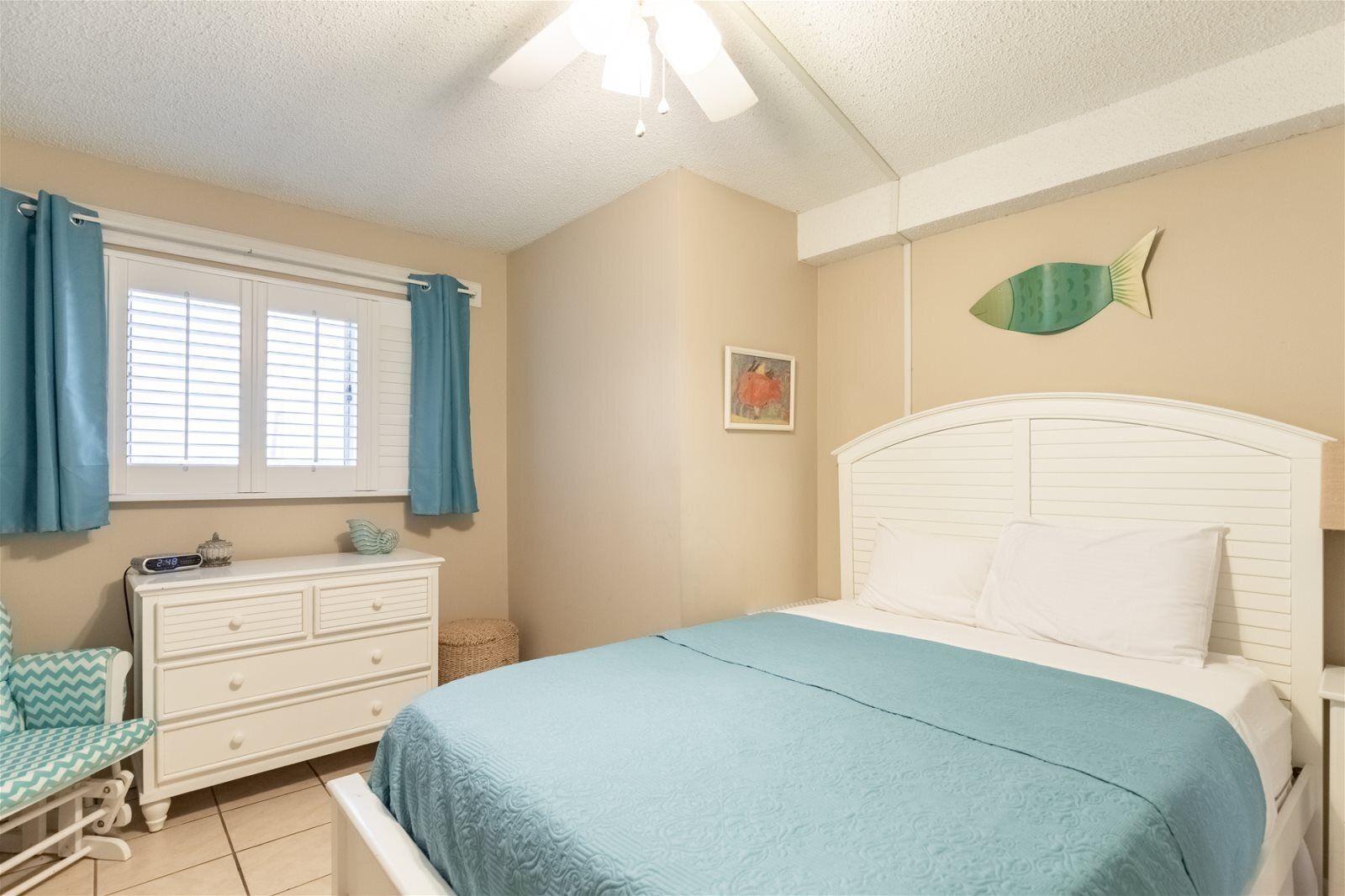 Un dormitorio con cama, cómoda, silla, ventana con cortinas y un adorno en la pared.