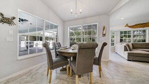 Un vaste espace dédié à la salle à manger, avec une table ronde et quatre chaises, de grandes fenêtres offrant une vue sur l’extérieur et un lustre moderne.