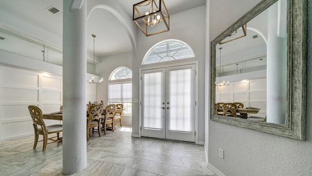 Une salle à manger spacieuse avec un haut plafond, des fenêtres en arc de cercle et un grand miroir au mur.