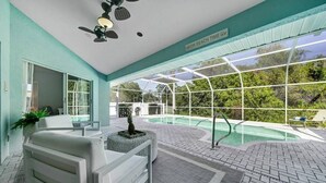 Un espace piscine intérieur moderne, doté d’une paroi vitrée, d’un ventilateur de plafond et d’un panneau indiquant : « C’EST L’HEURE DE SE DÉTENDRE À LA PLAGE ».
