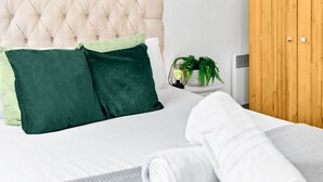 Un letto rifatto con cuscini verdi e bianchi, un asciugamano arrotolato di colore bianco e un comodino con una pianta e una lampada.