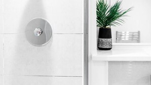 Un bagno con una parete rivestita di piastrelle bianche, uno specchio rotondo e una pianta in vaso su un piano di lavoro bianco.