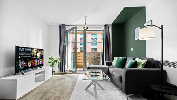Un soggiorno moderno con una TV a schermo piatto, un divano, un tavolino da caffè in vetro e vista su un edificio attraverso una porta scorrevole in vetro.