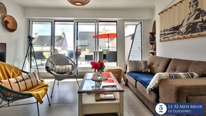 A modern living room with a glass coffee table, a sofa, a chair, and a large window with a view of the city. - 30 m2 terrace with sea view, 40 m from the beach and 300 m from shops (Guilvinec)