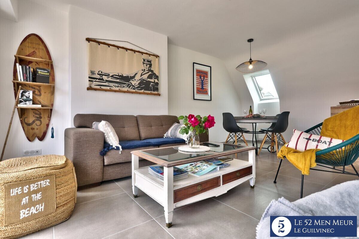 Ein modernes Wohnzimmer mit einer Couch, einem Couchtisch und einem Bücherregal. Es gibt einen Essbereich mit Tisch und Stühlen.