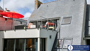 A residential building with a grey tiled roof, a balcony with a red umbrella, and a visible window. - 30 m2 terrace with sea view, 40 m from the beach and 300 m from shops (Guilvinec)