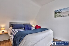 A neatly made bed with striped bedding and two pillows, a bedside lamp, and a framed artwork on the wall.